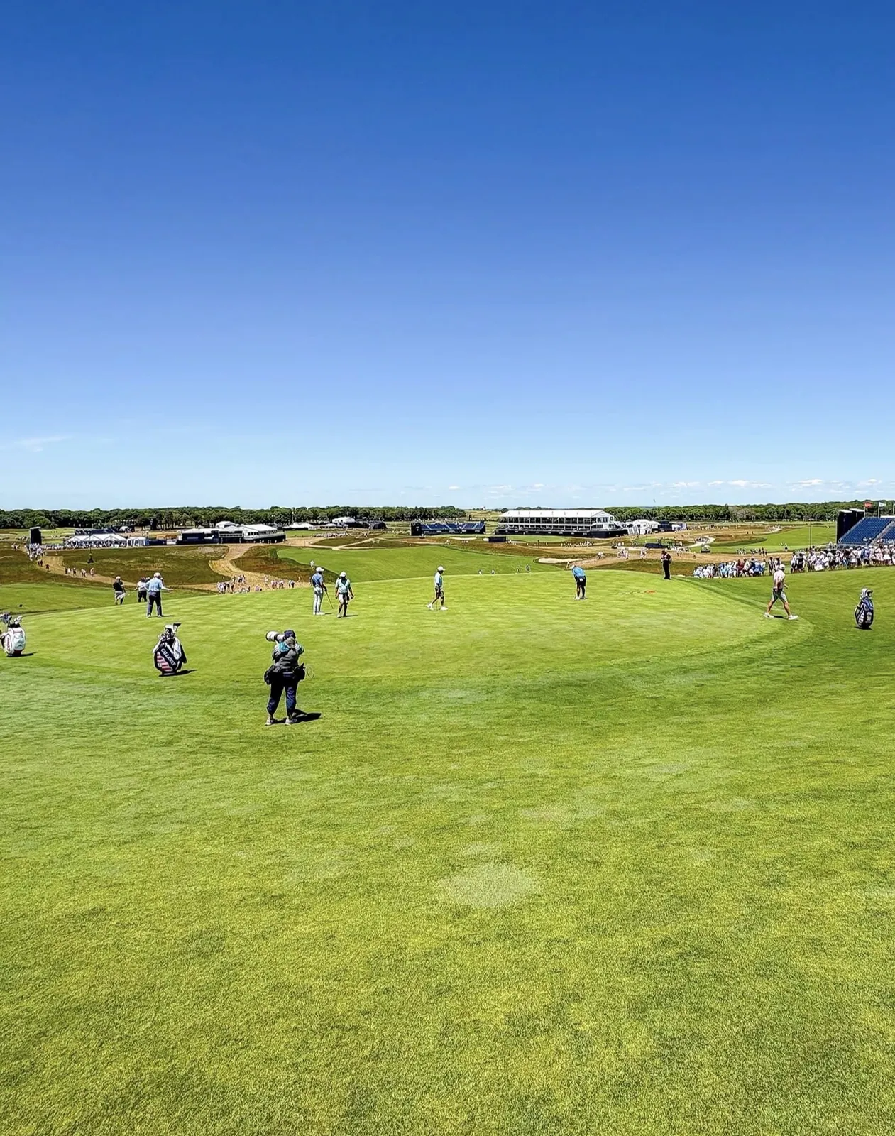 US Open practice round with players walking a fairway and a USA-flag Callaway caddie bag in the foreground