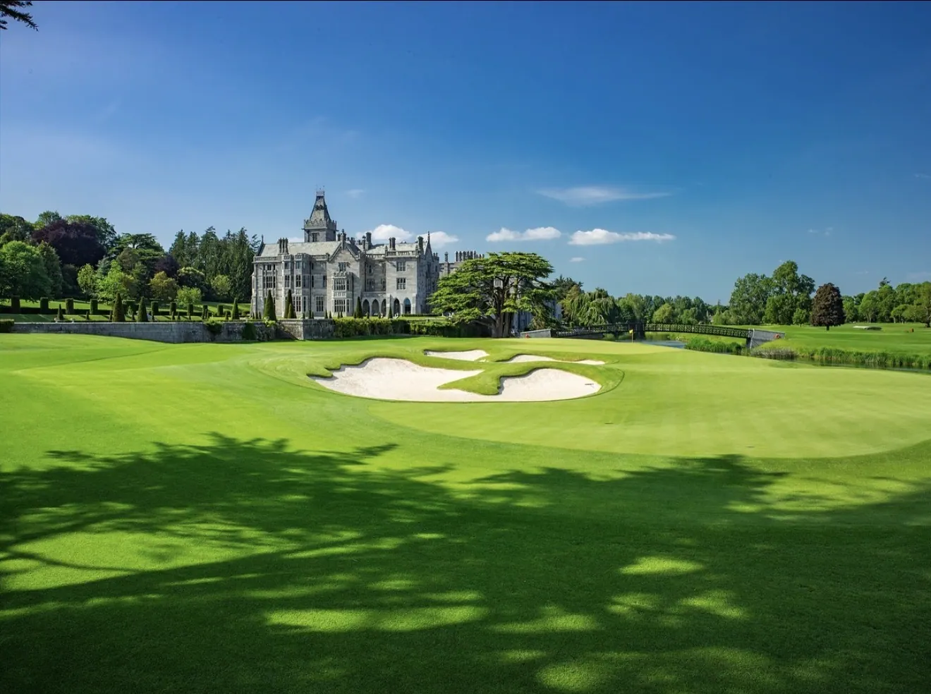 Adare Manor stone castle behind a golf green with a clover-shaped white sand bunker