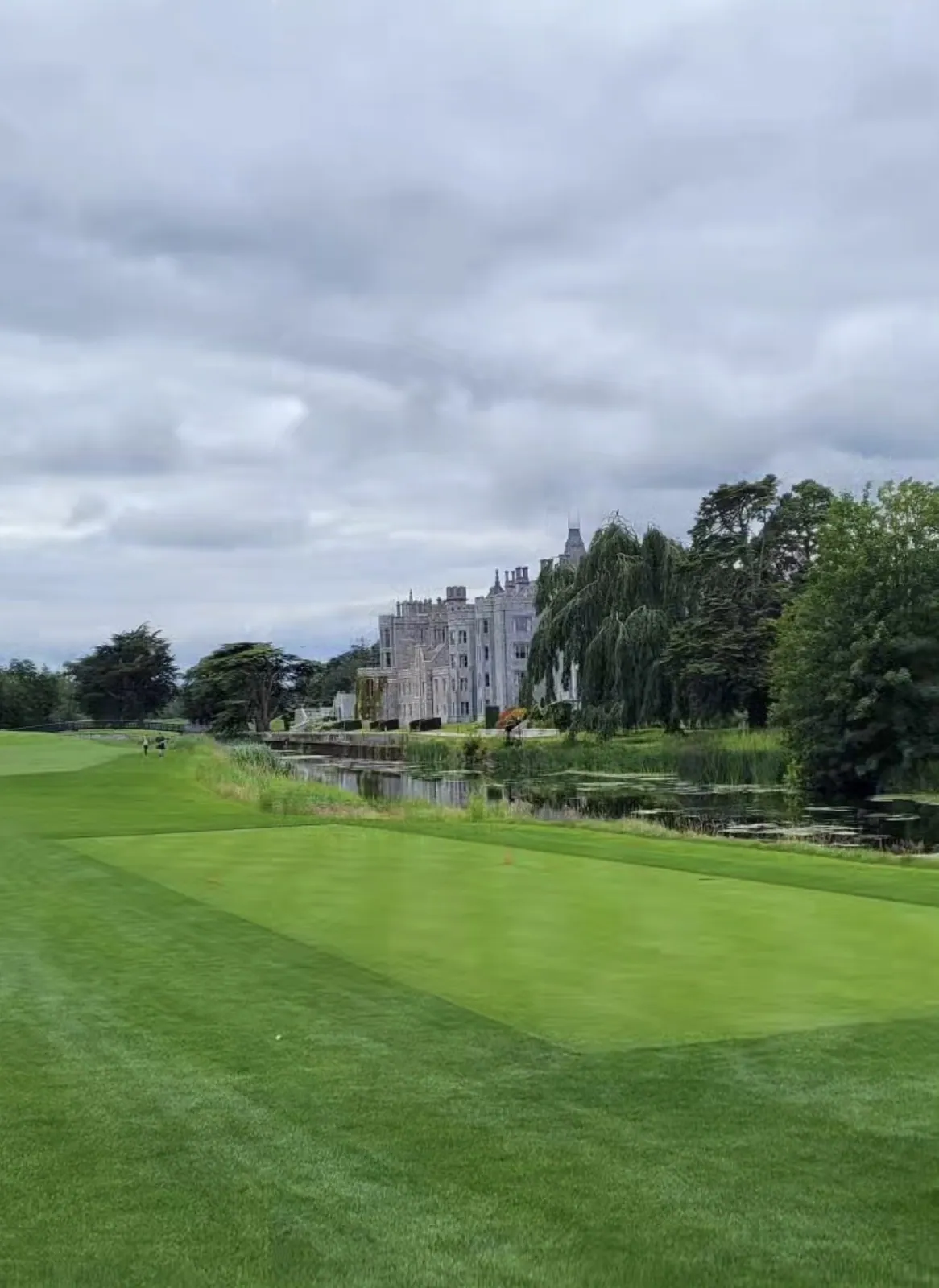 Adare Manor house seen across the river from a manicured fairway under grey skies