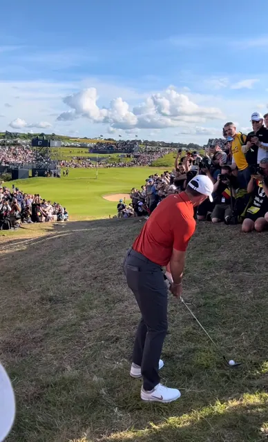 Golfer in red shirt playing a chip beside a large crowd of photographers at Royal Portrush