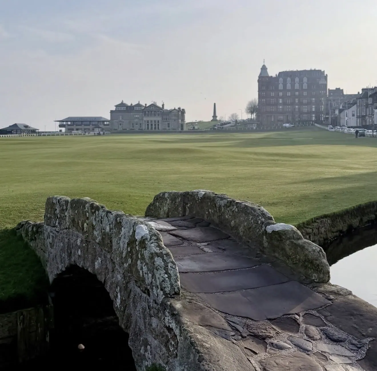 The stone Swilcan Bridge on the Old Course at St Andrews with the R&A clubhouse and Hamilton Grand beyond